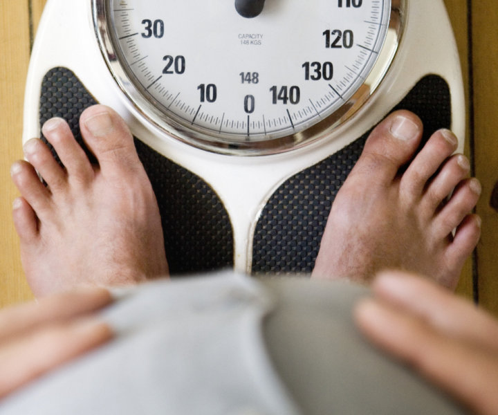 Man holding belly, with feet on weighing scales